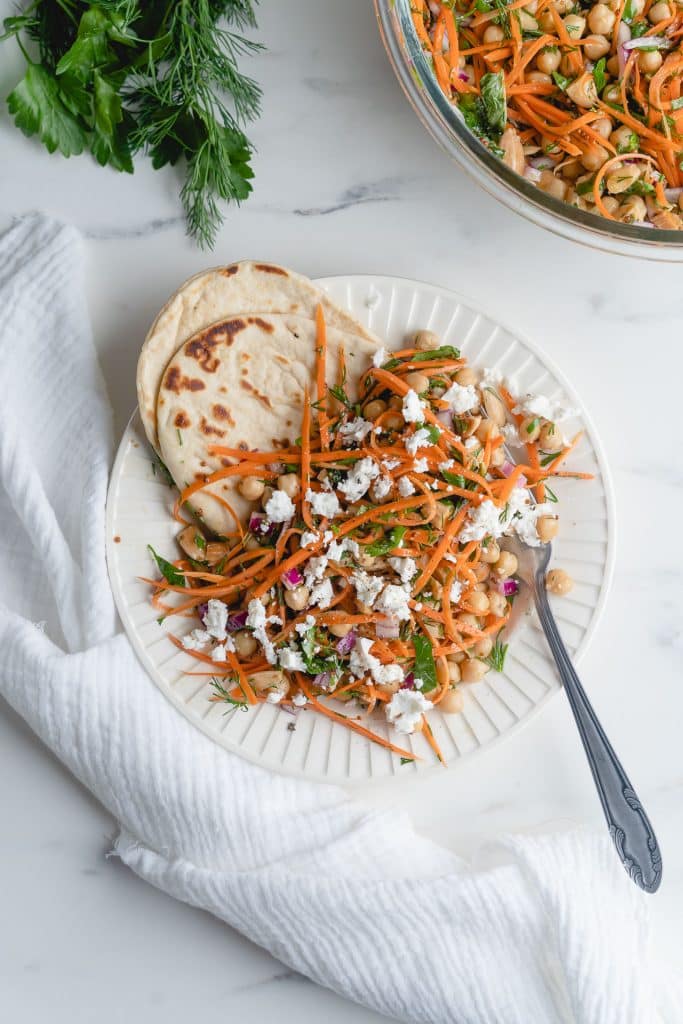 Top view of a plate of grated carrot and chickpea salad on a white background