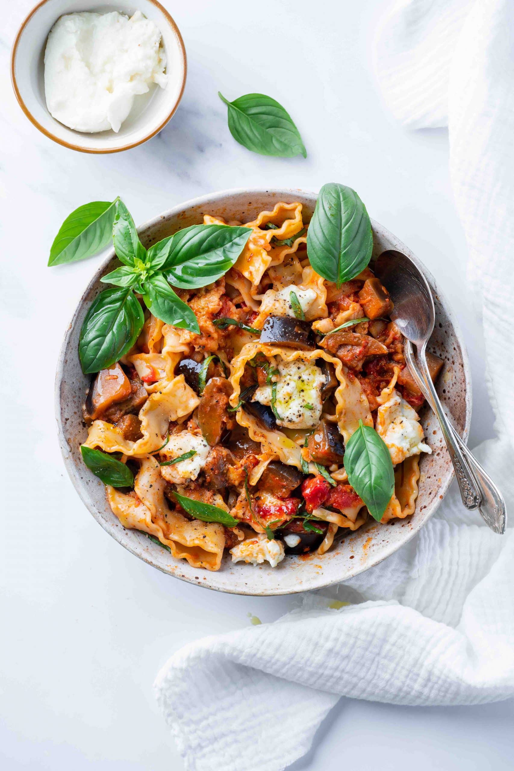 Top view of a bowl of eggplant and mozzarella pasta decorated with basil leaves