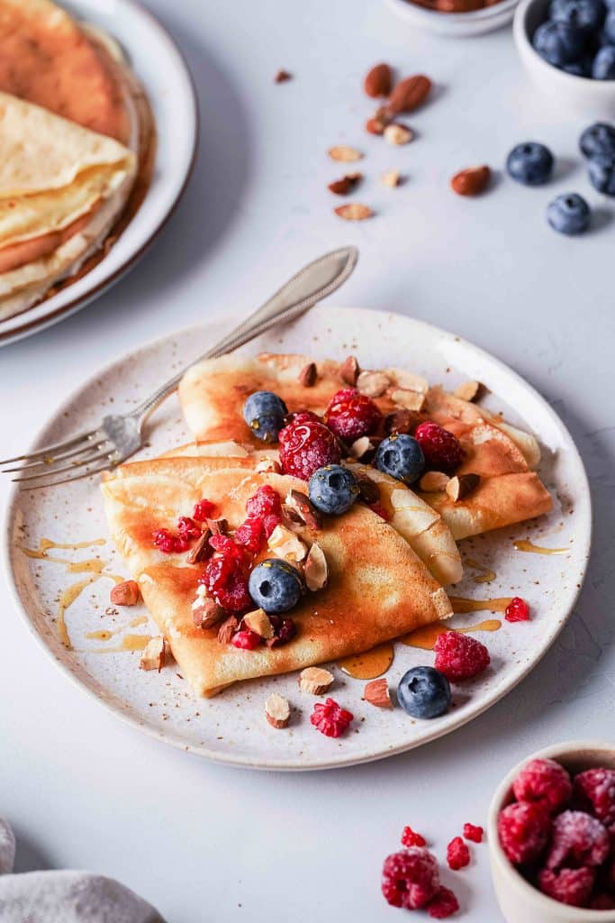 Zoom on a plate of two almond milk crepes served with berries and almonds