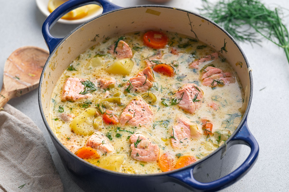 Finnish salmon soup with chunks of fish, potatoes, carrots, and fresh dill in a blue enameled cast iron pot.