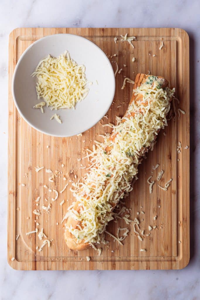 Top view of an unbaked baguette garlic bread with cheese.