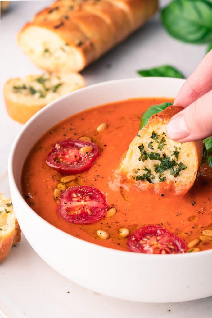 a person dipping a piece of bread into a bowl of tomato soup.	