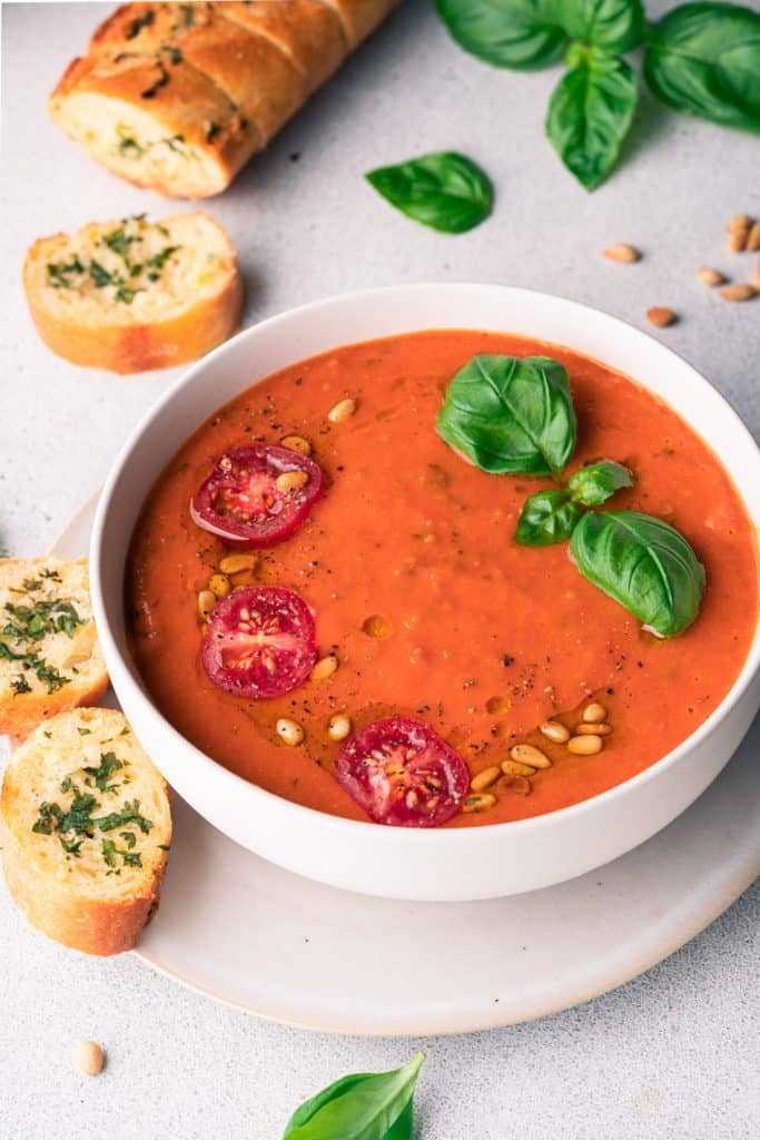 A bowl of tomato soup decorate with basil, tomatoes and pine nuts.