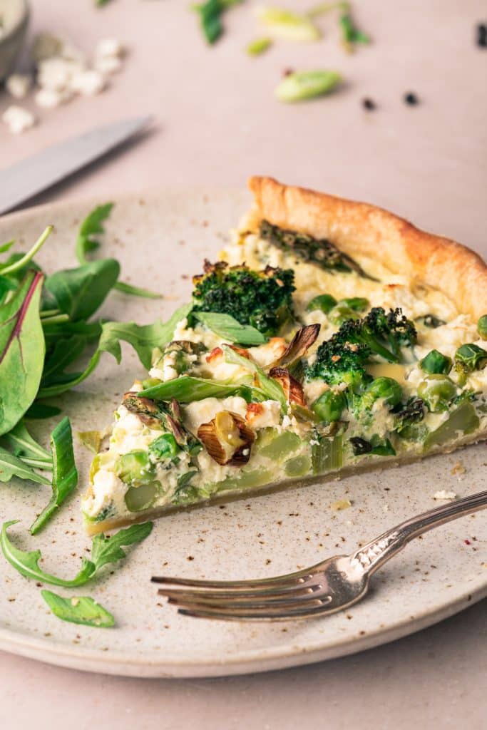 Slice of spring quiche with asparagus, broccoli and peas on a plate.