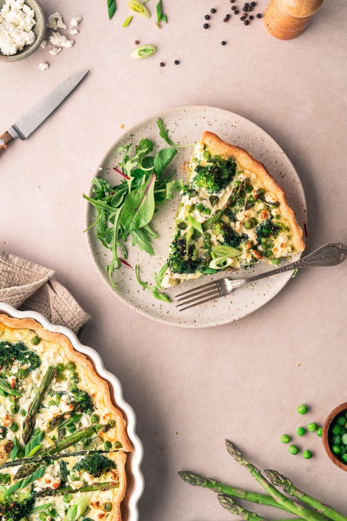 Slice of spring quiche with asparagus, broccoli and peas on a plate.