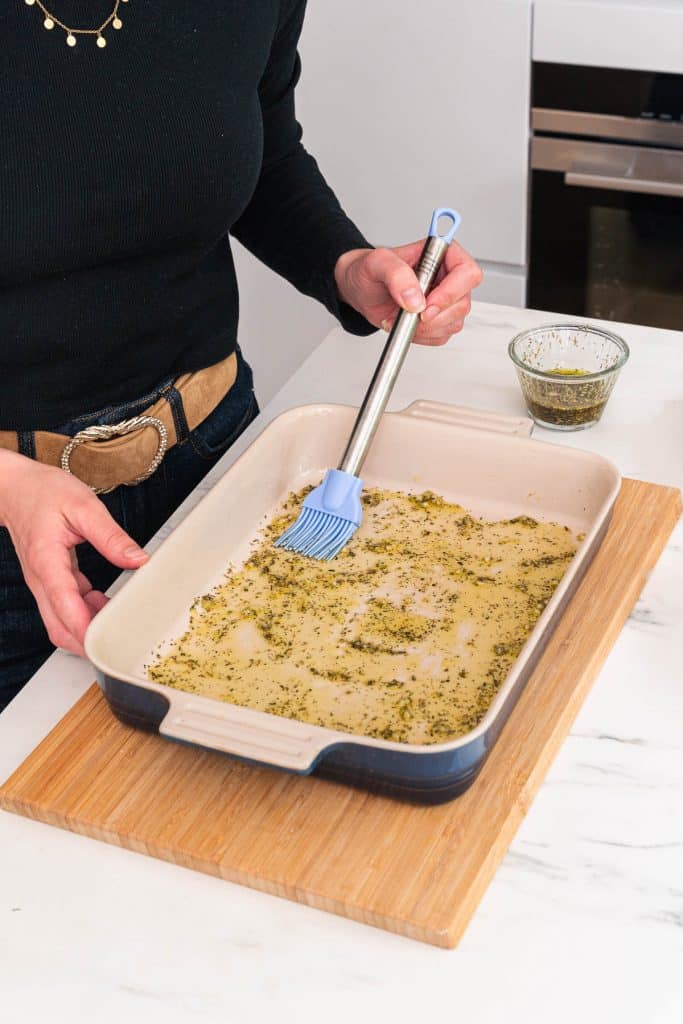 Someone brushing a baking dish with a mix of olive oil and herbs