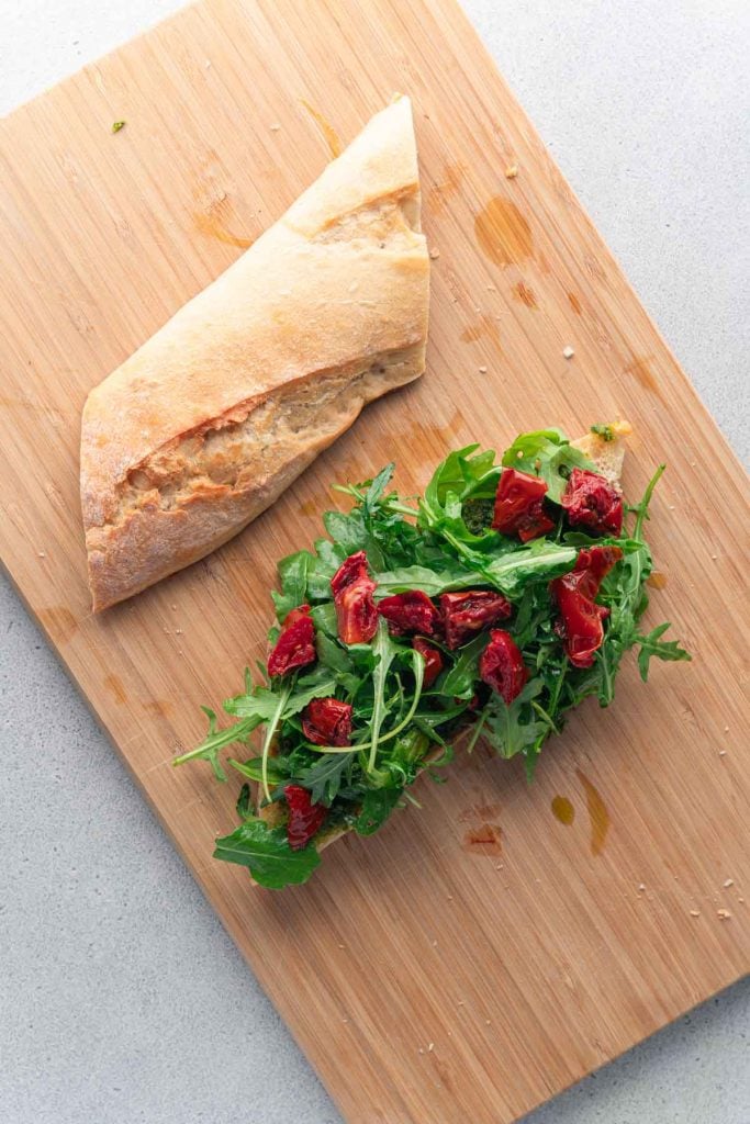 Ciabatta halves layered with pesto, arugula and sun-dried tomatoes 