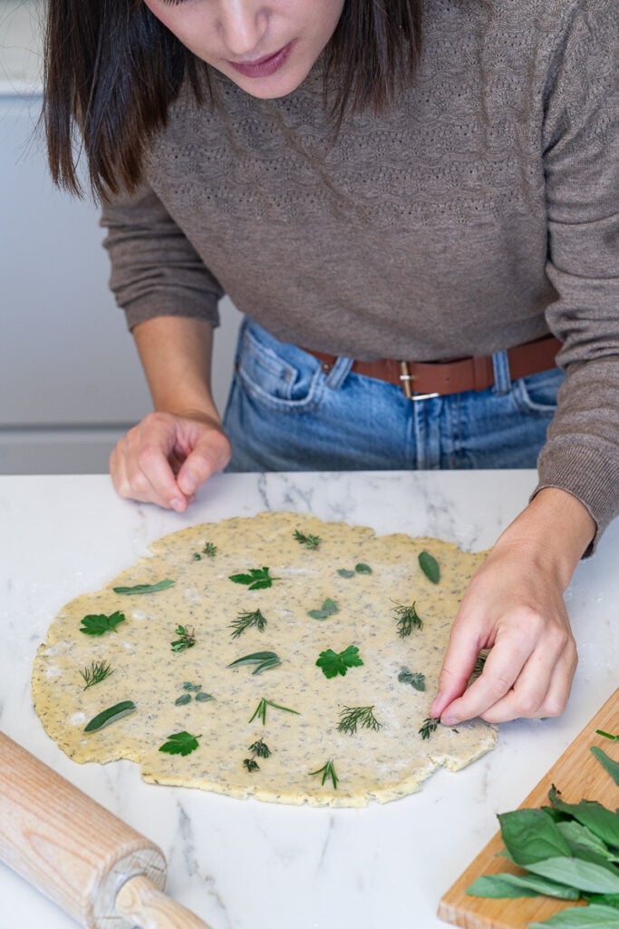Someone placing fresh herbs on a savory Parmesan cookies dough