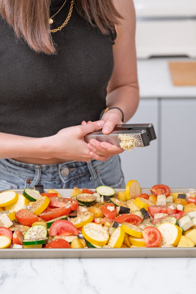 Person grating garlic on a platter of assorted sliced vegetables, including tomatoes, zucchini and squash.