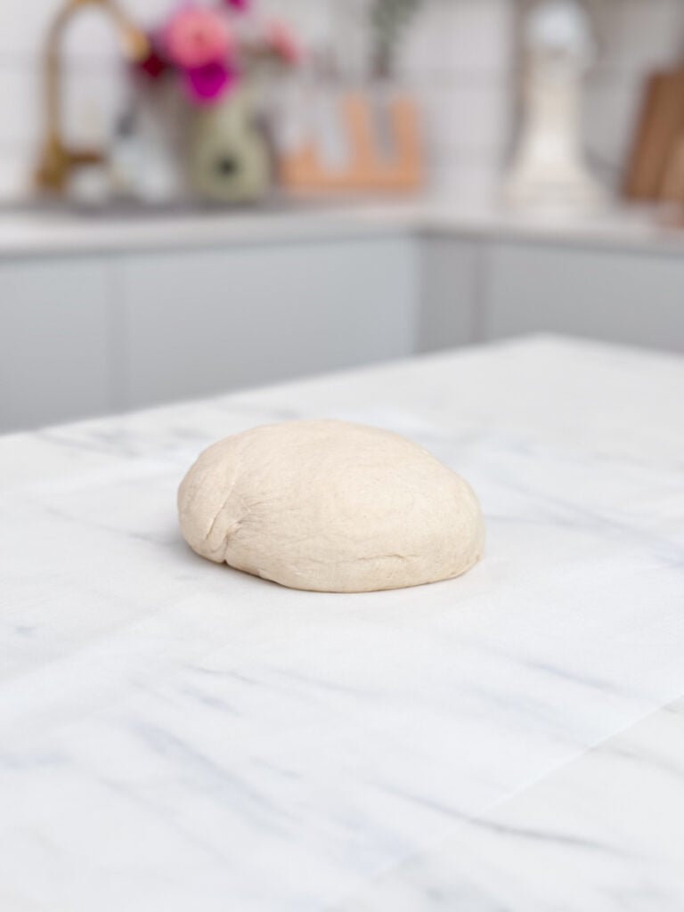 Une boule de pâte à pizza sur un plan de travail en marbre pour réaliser une pissaladière niçoise.