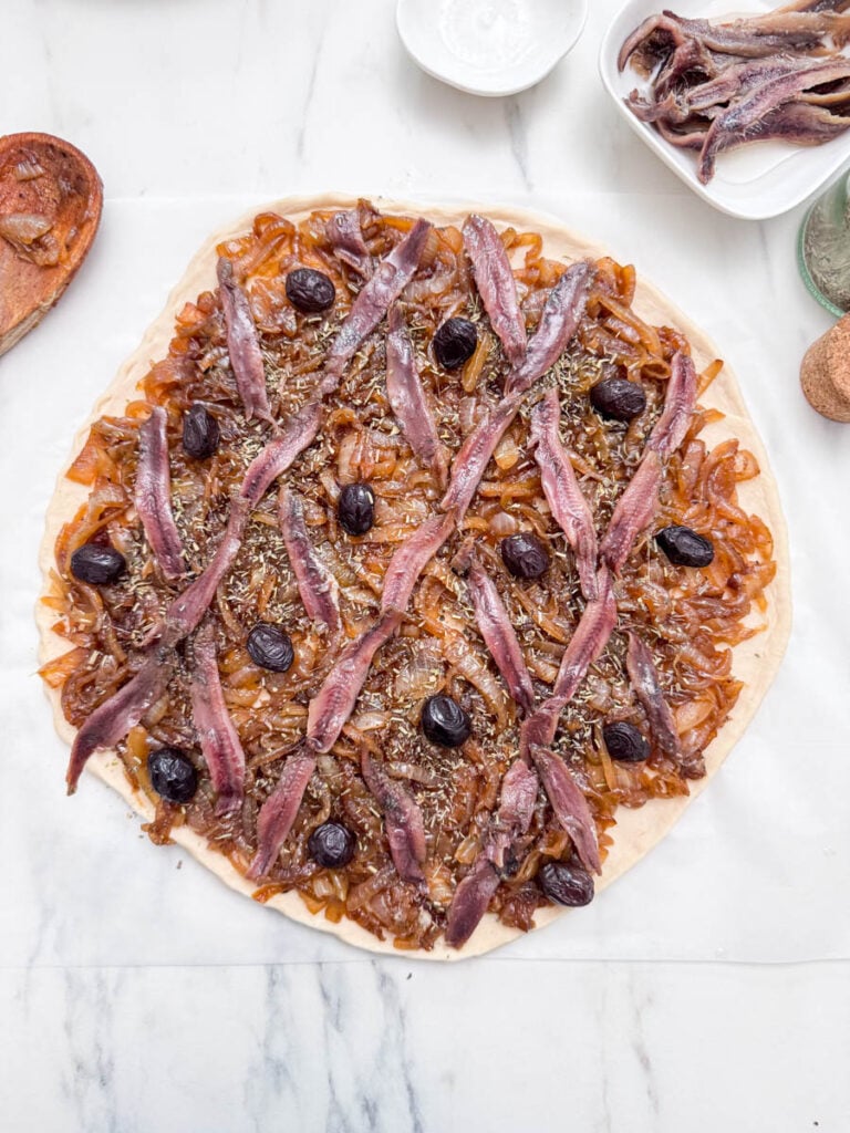 Une pissaladière niçoise, garnie d'oignons caramélisés, de filets d'anchois disposés en treillis et d'olives noires avant la cuisson.