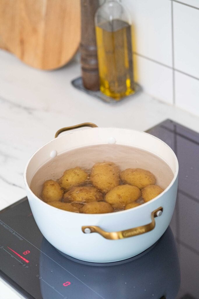 Une marmite blanche remplie de pommes de terre entières bouillantes sur une table de cuisson à induction.