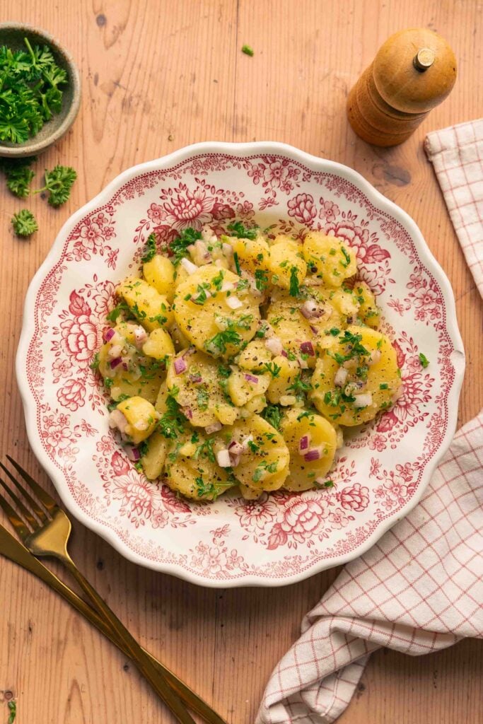 Ein Teller mit elsässischem Kartoffelsalat mit Petersilie, roten Zwiebeln und Vinaigrette, der auf einem Holztisch steht.