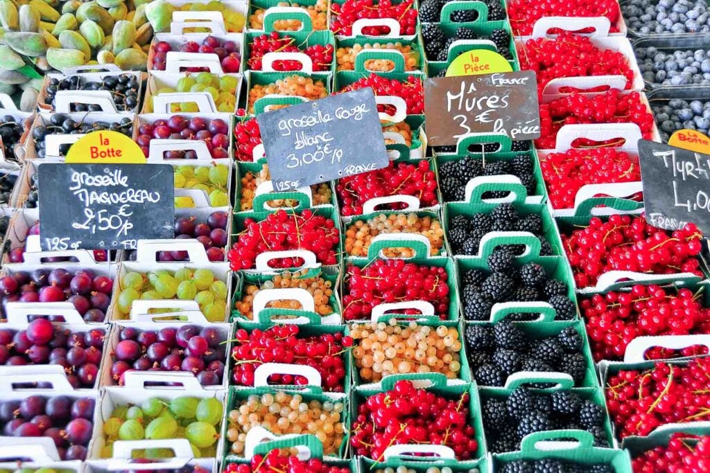 Eine Auswahl an Beeren und Früchten in grünen Kartons, die auf einem Marktstand mit handgeschriebenen Preisschildern ausgestellt sind.