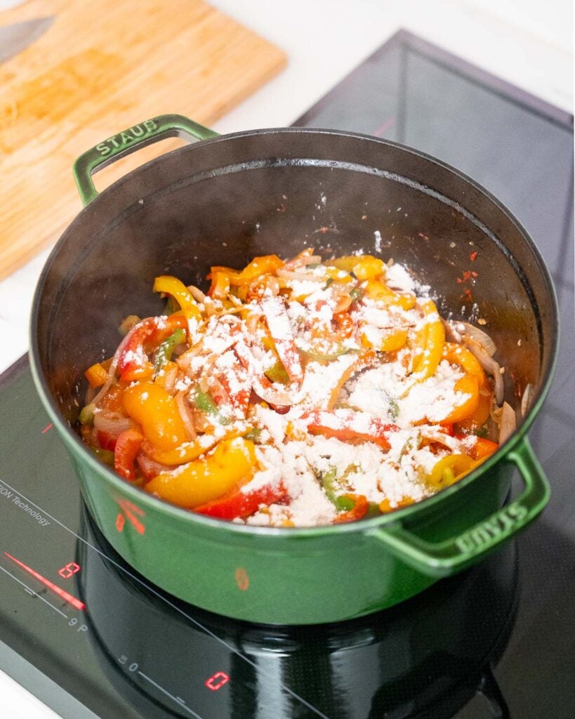 A green saucepan on an induction stove contains a colorful mixture of sautéed vegetables and flour on top.