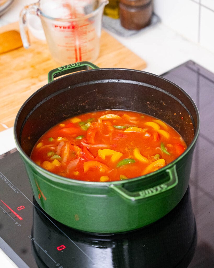 In einem grünen Topf auf dem Herd steht eine Piperade-Sauce, mit der Sie ein Hühnchen Basquaise zubereiten können.