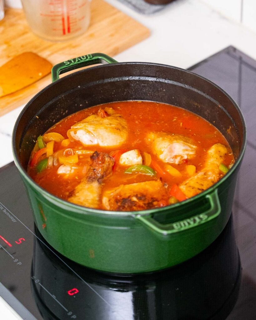 Une casserole verte sur une cuisinière avec du poulet basquaise en préparation.