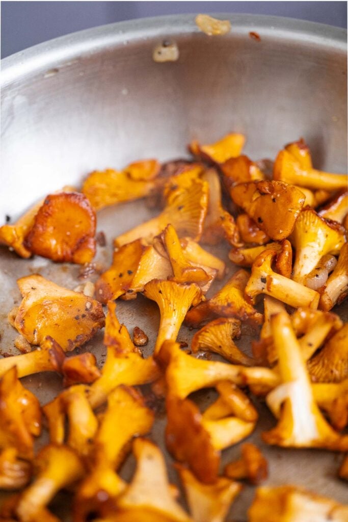 A stainless steel pan filled with sautéed orange and brown chanterelle mushrooms.