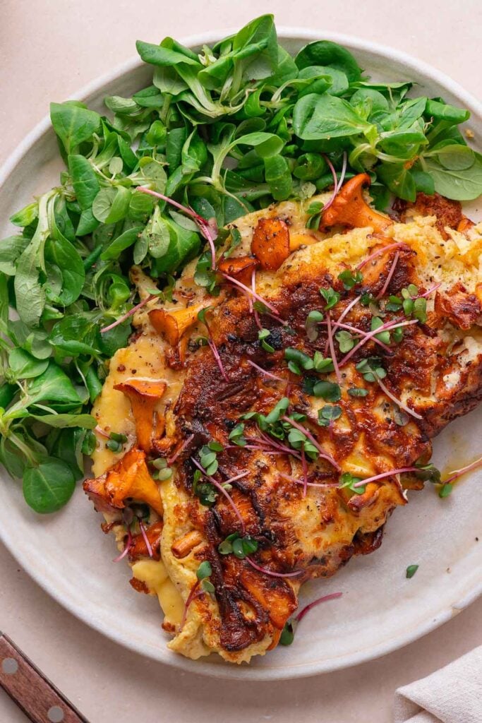 Omelette aux herbes et légumes grillés, servie avec une salade verte fraîche sur une assiette blanche.