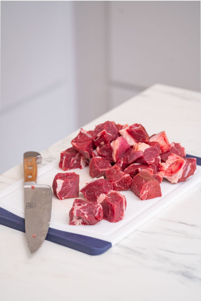 Pieces of raw meat on a cutting board next to a knife.