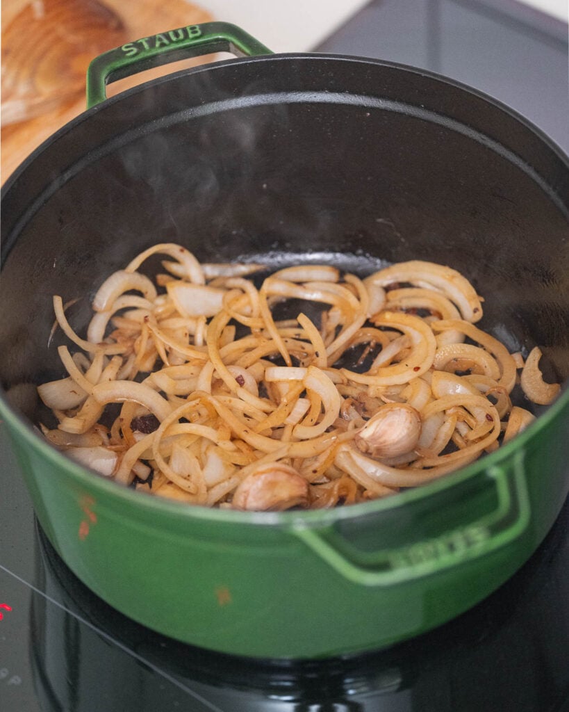 Chopped onions and garlic cloves sautéed in a green saucepan on a stovetop.