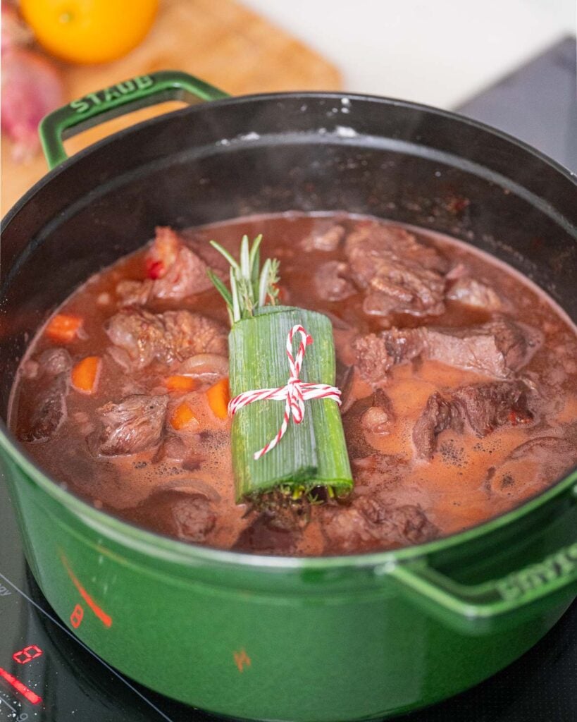 A green beef stew with carrots and herbs cooking on a stovetop.