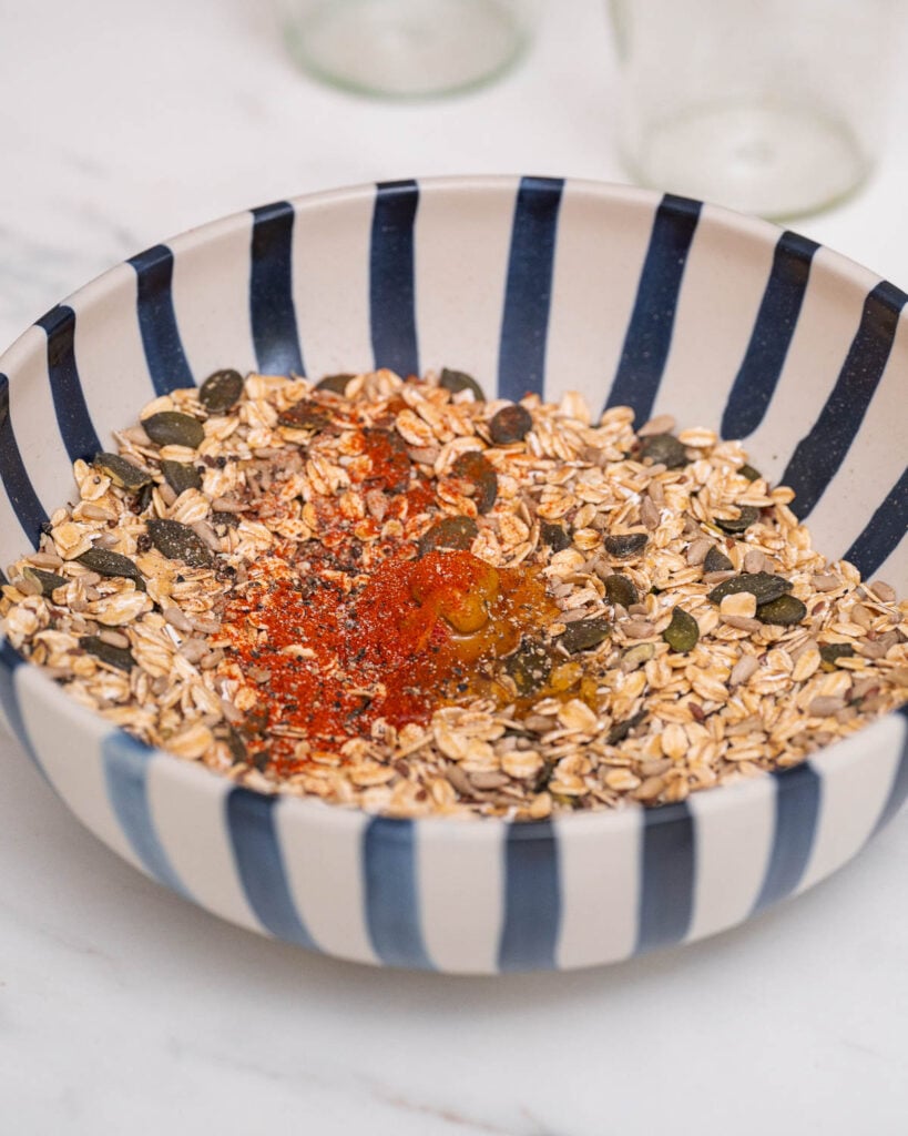 A blue and white striped bowl containing oats, pumpkin seeds, spices and a small amount of liquid.