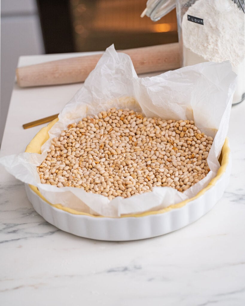 Une pâte brisée avant d'être précuite pour préparer une quiche poireaux chèvre lardons sur un plan de travail en marbre.