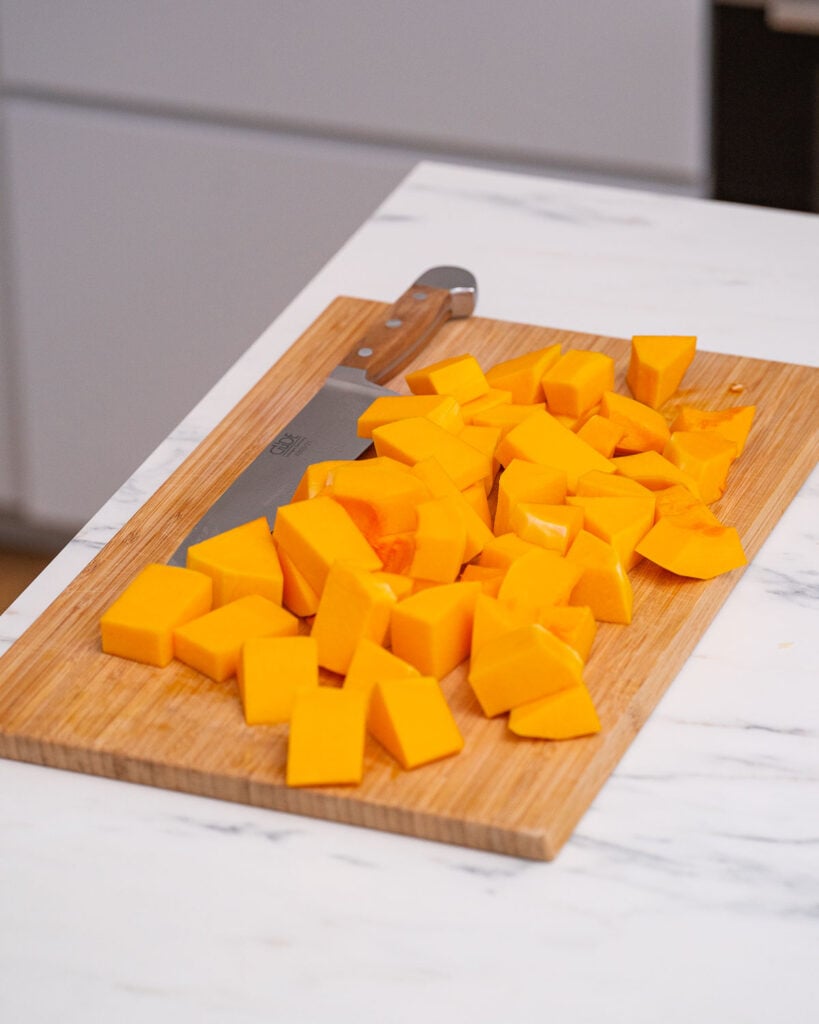 The chopped butternut squash, ready to be transformed into a delicious butternut velouté, is placed on a wooden cutting board next to a sharp knife.