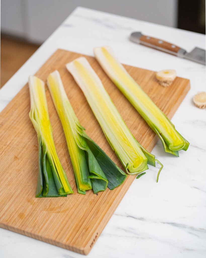 Sliced leeks on a wooden cutting board next to a knife on a marble work surface.