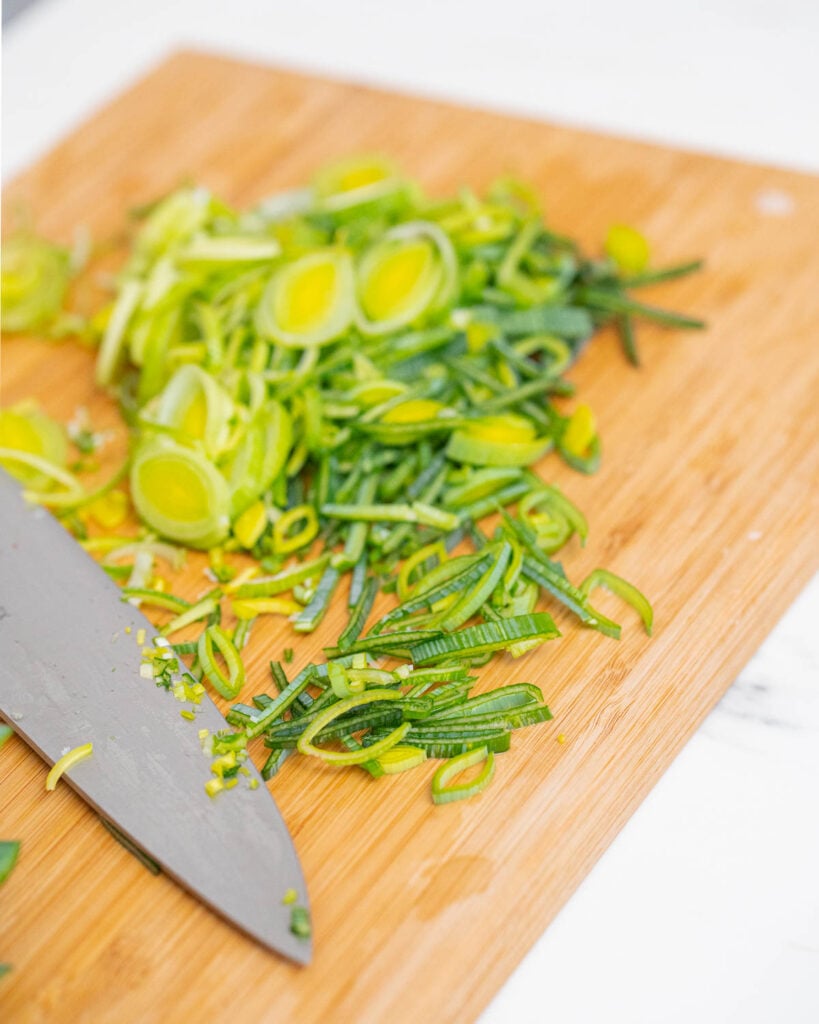 Grüne Zwiebeln, die auf einem Holzbrett mit einem Kochmesser in Scheiben geschnitten wurden, eignen sich hervorragend für die Zubereitung einer Lauch-Kartoffel-Suppe.