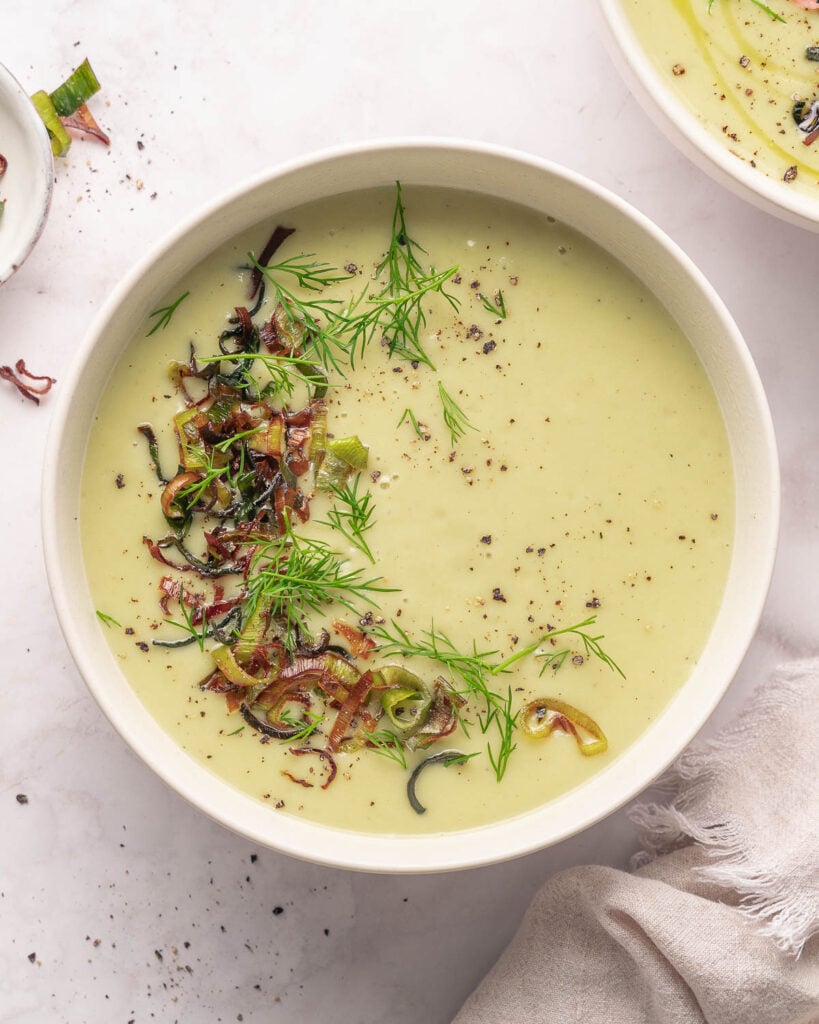 Bowl of creamy soup topped with herbs and crispy onions on a light surface.