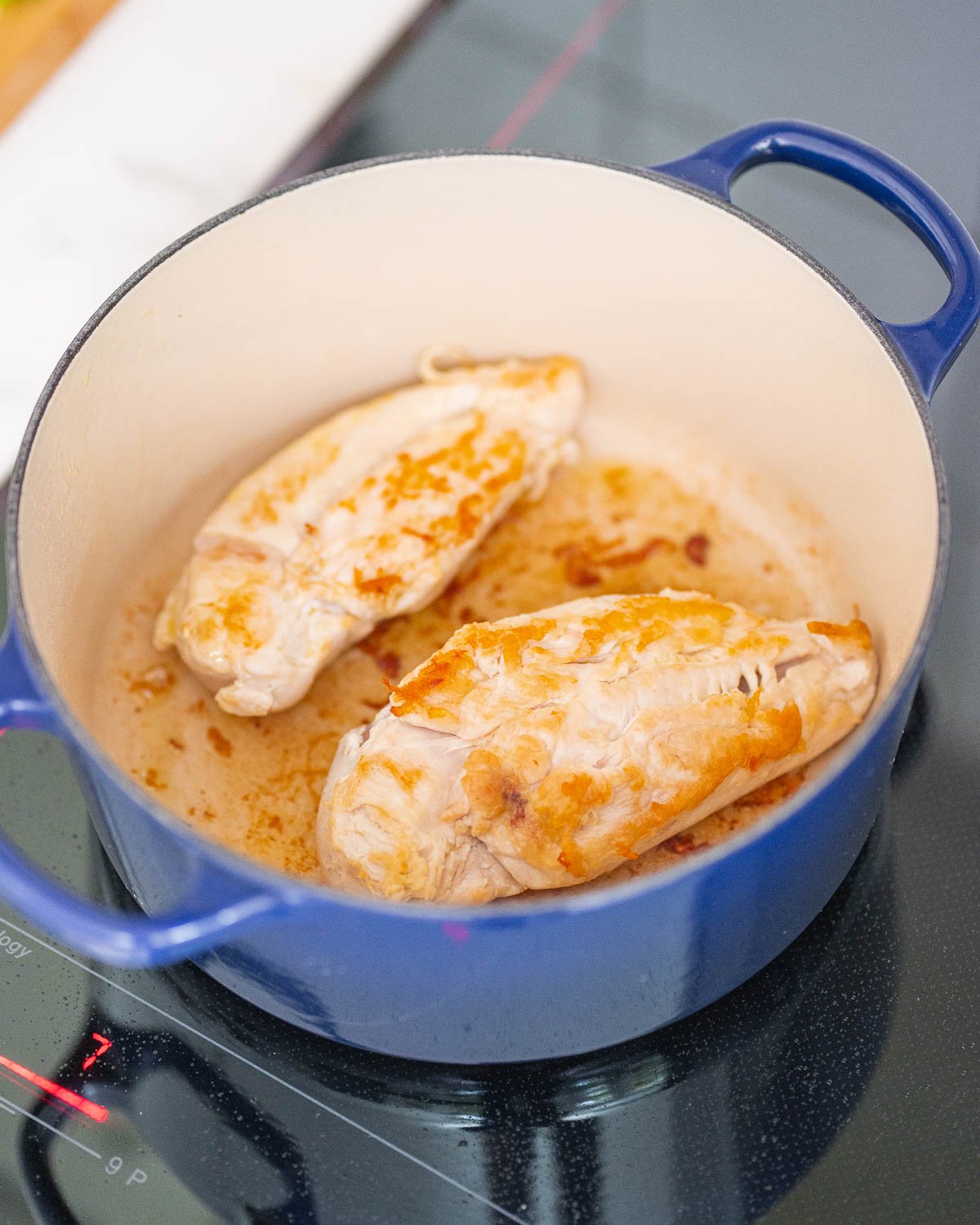 Two chicken breasts cooked in a blue pan on a stovetop.