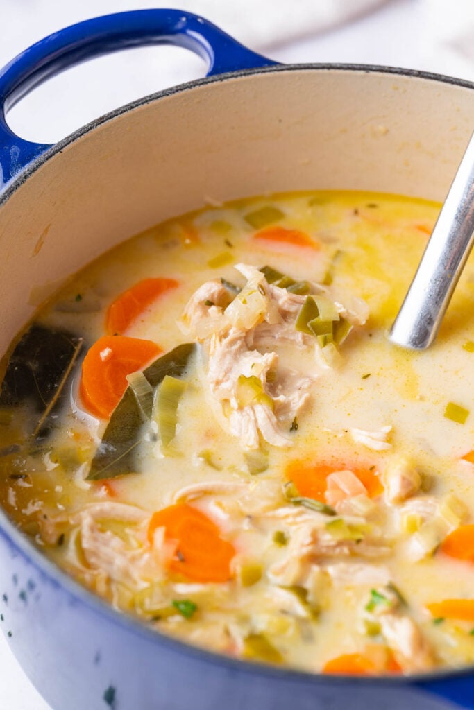 A creamy vegetable chicken soup casserole with visible chicken pieces, sliced carrots and greens, stirred with a metal spoon.