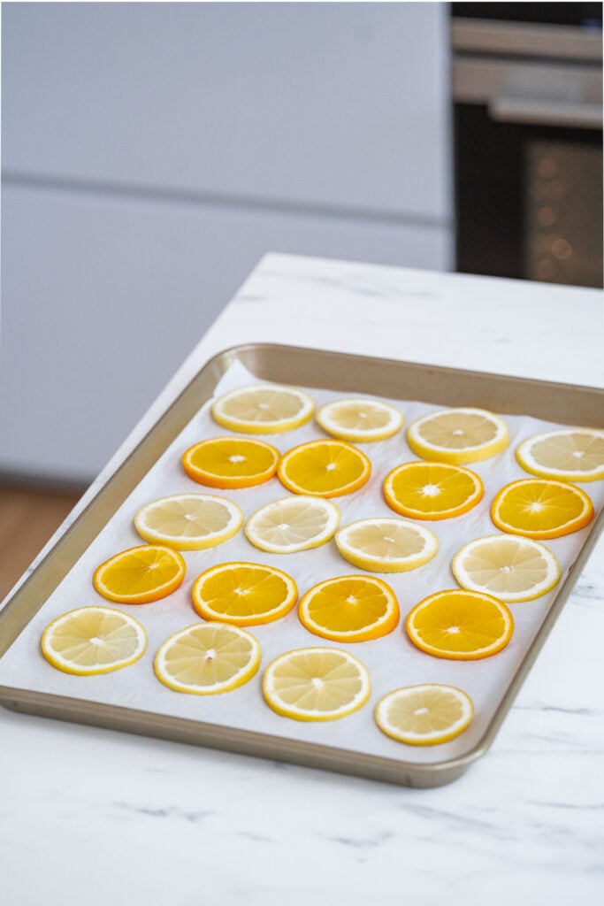 Arrange sliced oranges and lemons on a parchment-lined baking sheet.