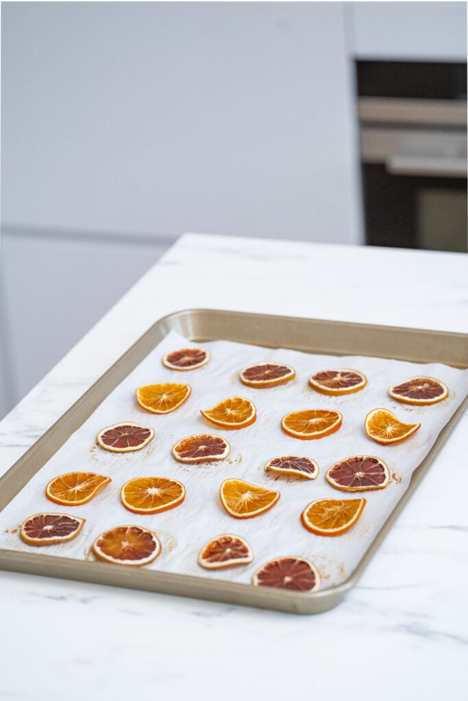 A baking sheet with dried orange and grapefruit slices carefully arranged and evenly spaced on parchment paper.