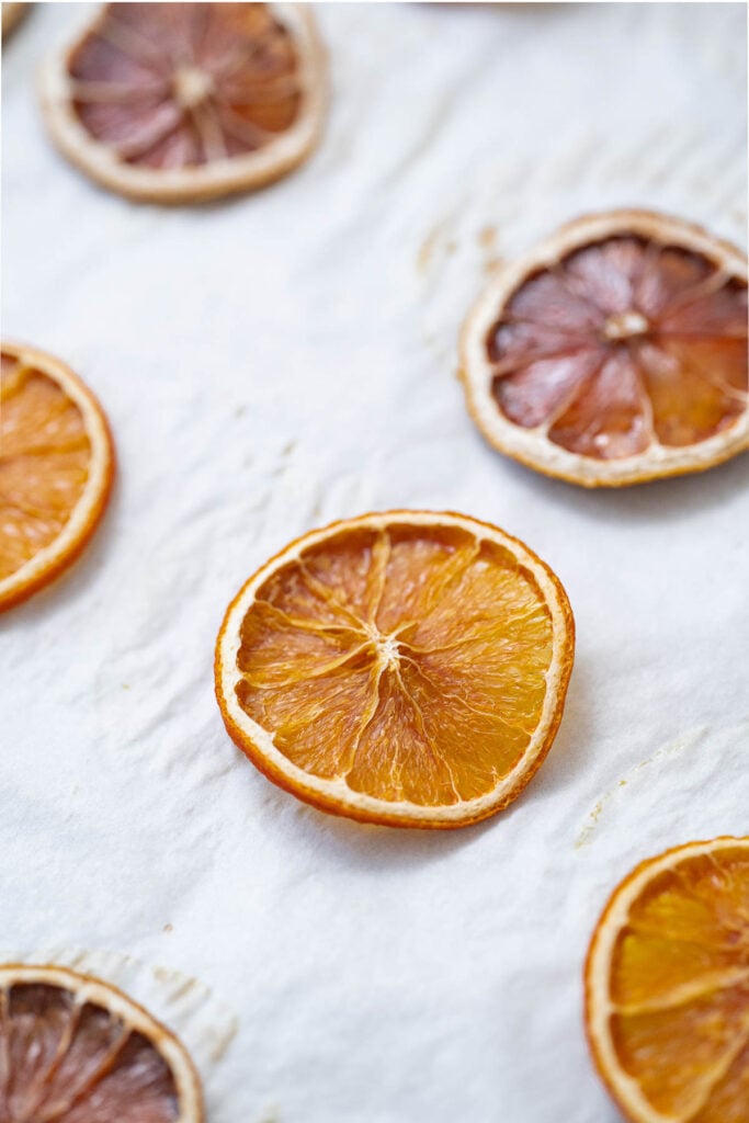 Dried oranges sliced on a white surface, arranged in a scattered pattern.