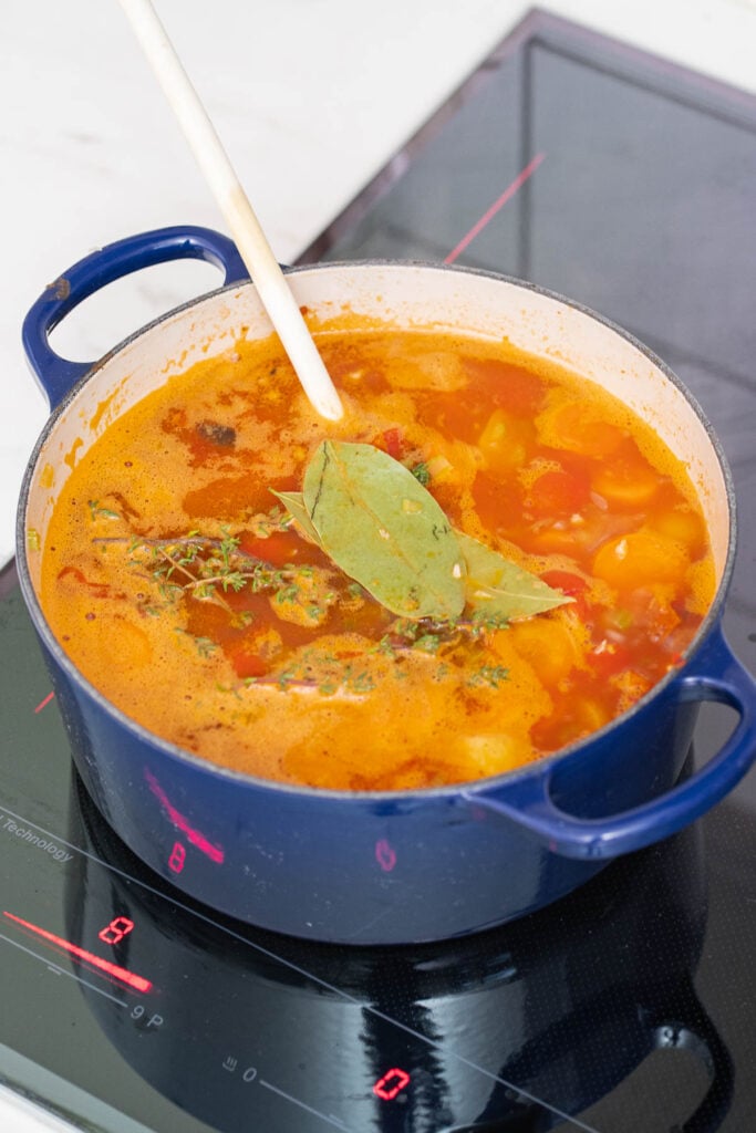 Une casserole bleue sur la cuisinière électrique contient une soupe mijotée de haricots blancs, de tomates avec des herbes et une feuille de laurier, doucement remuée avec une cuillère en bois.