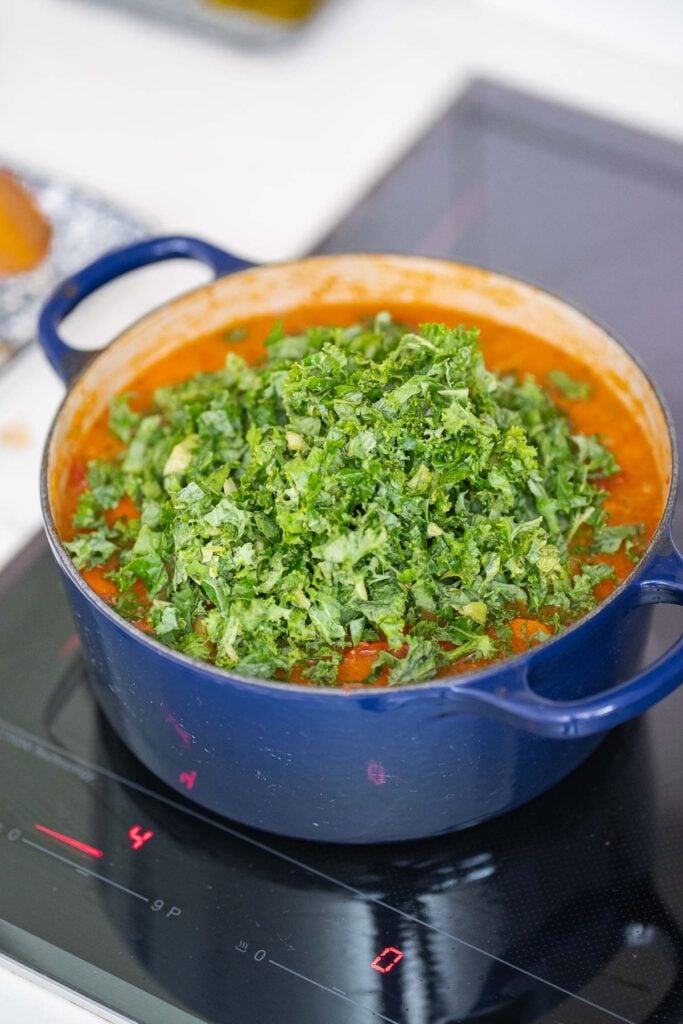 Une casserole bleue sur la cuisinière contient une savoureuse soupe de haricots blancs à la tomate, richement infusée d'un ragoût à base de tomates et garnie de chou frisé frais haché.