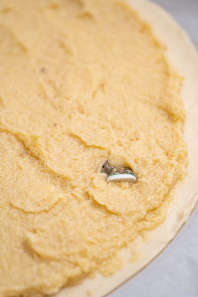 A close-up of a tart crust filled with a creamy yellow pastry, evoking a French Tradition. A small metallic object stands out, reminiscent of the surprise of a Galette des Rois. 