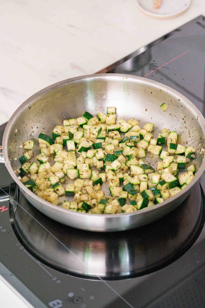 Courgettes en dés sautées dans une casserole en acier inoxydable sur une cuisinière électrique.