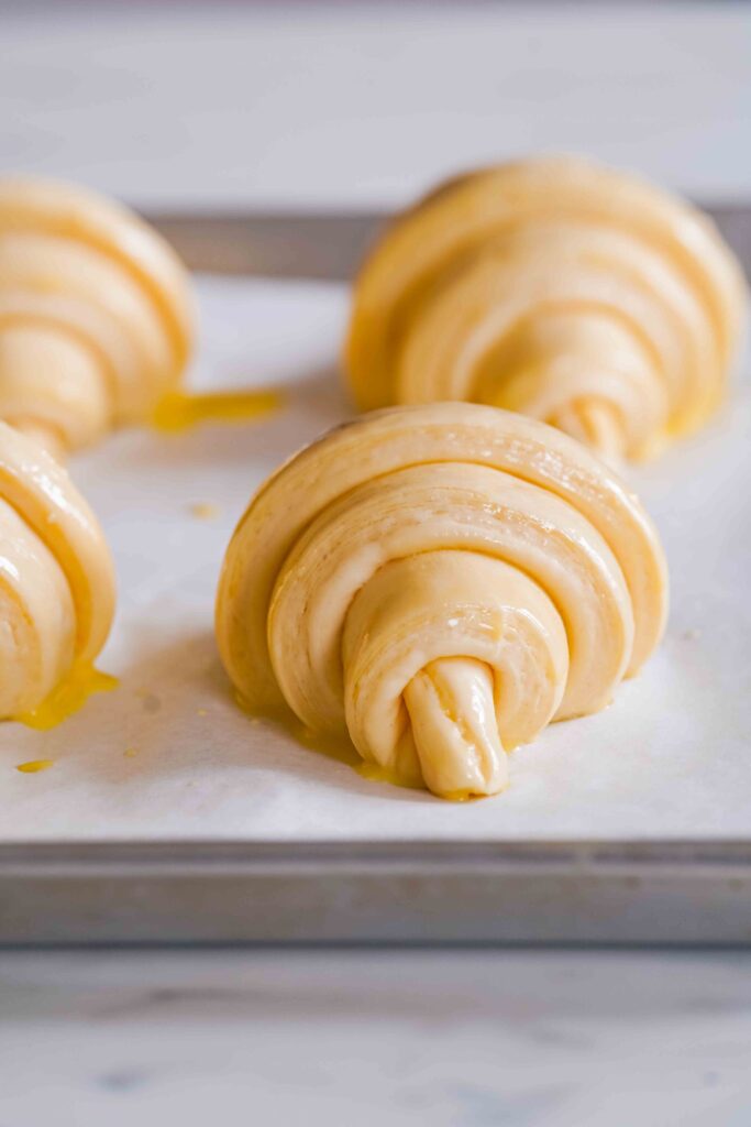Unbaked croissants are placed on a parchment-lined baking sheet, ready to be baked.