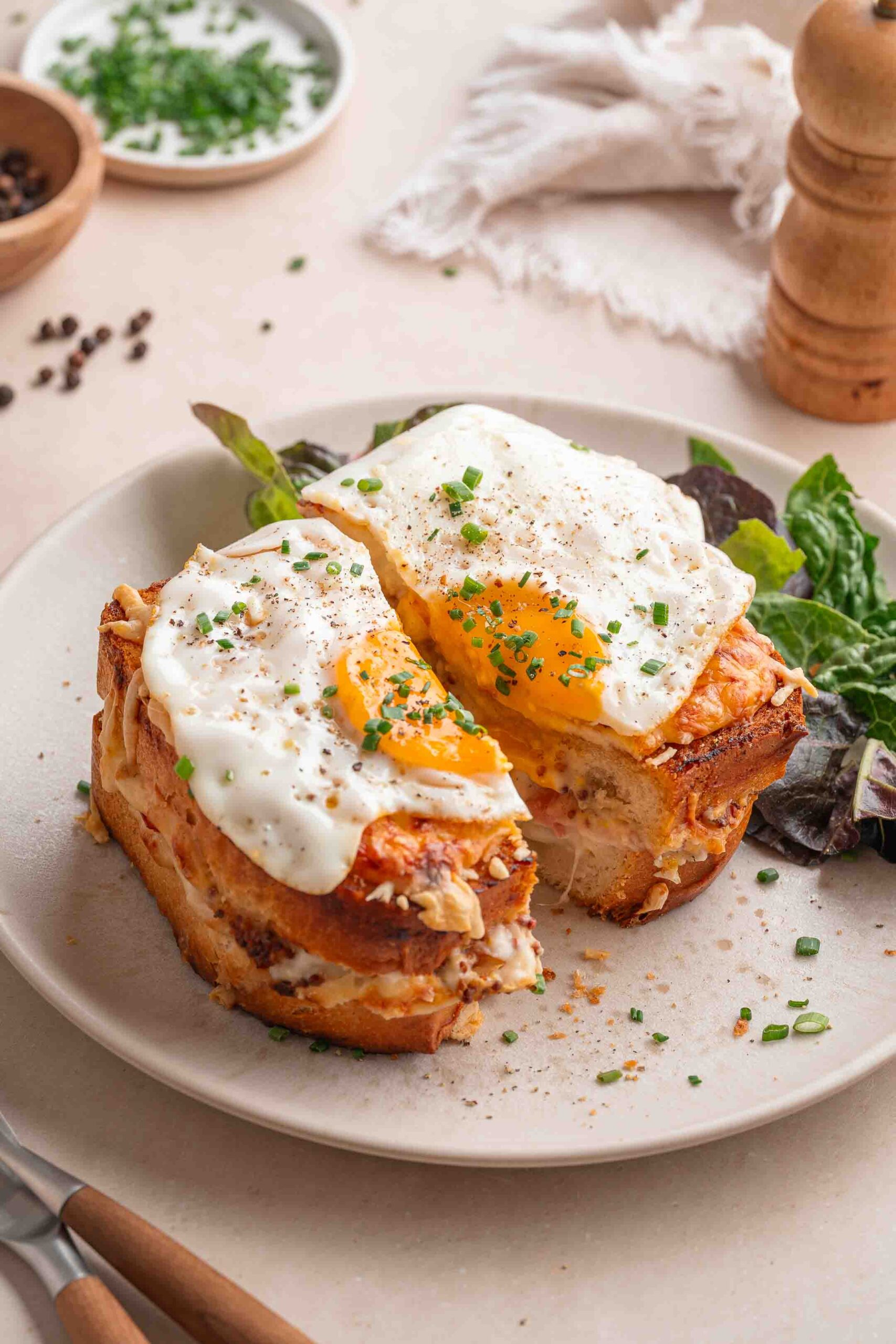 Ein Teller mit einem Sandwich, das mit zwei gekochten Eiern belegt, mit gehacktem Schnittlauch dekoriert und mit gemischten Salaten serviert wird.