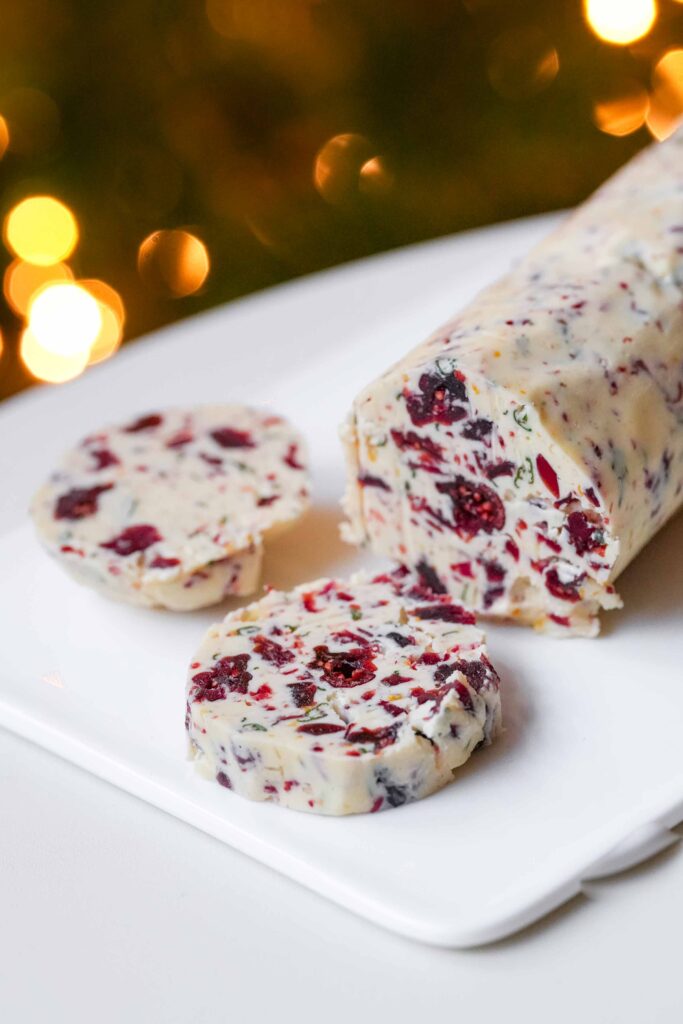 Un morceau de beurre de Noël - un mélange de beurre avec des herbes et des canneberges séchées - est coupé en tranches et présenté sur une assiette blanche.