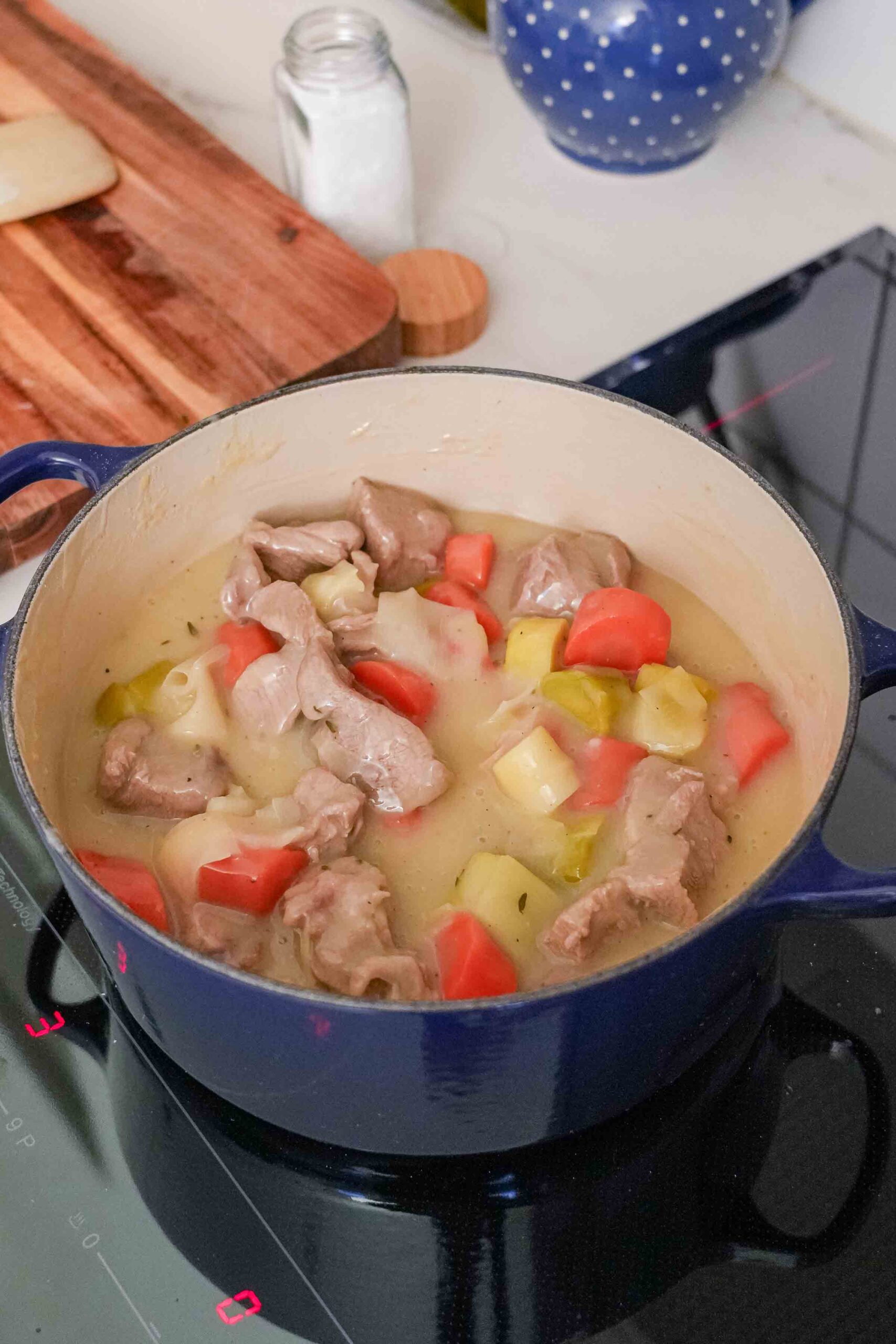 A blue pot on the stove contains a French veal stew with pieces of meat, potatoes and tomatoes in a light broth.