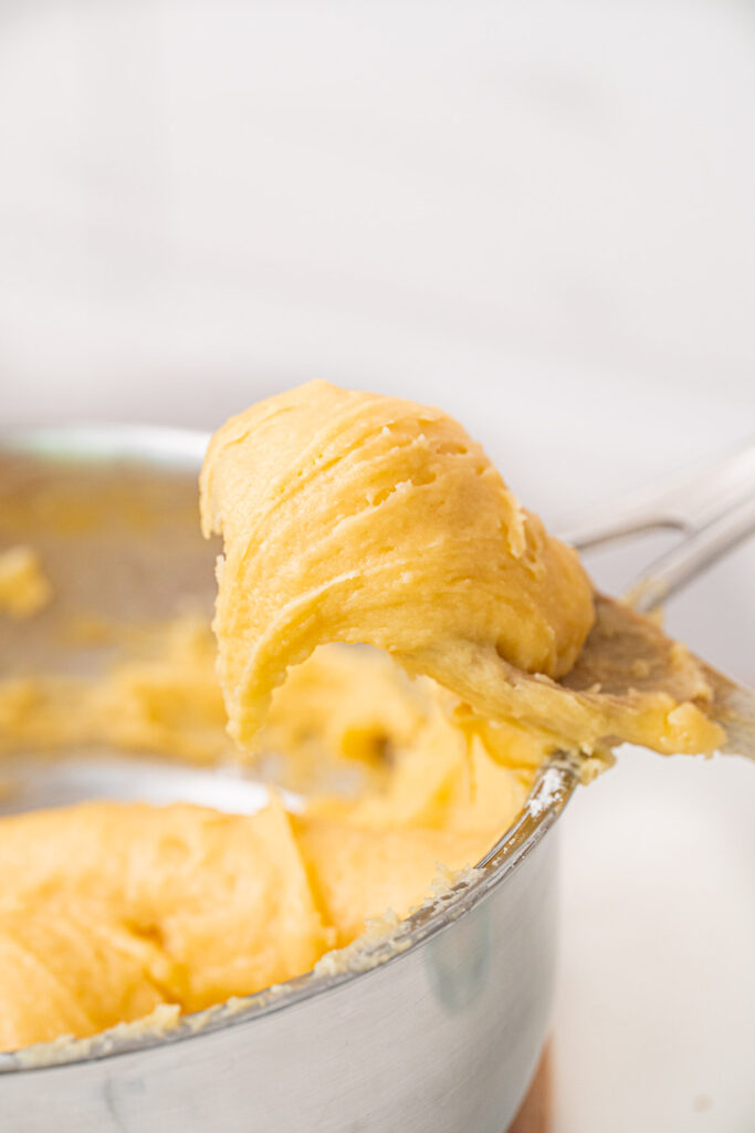 Close-up of a metal spoon scooping choux pastry out of a saucepan.