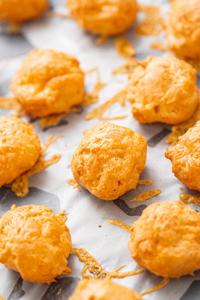 Golden cheese bites arranged on a baking sheet lined with parchment paper, with a little melted cheese visible around the edges.