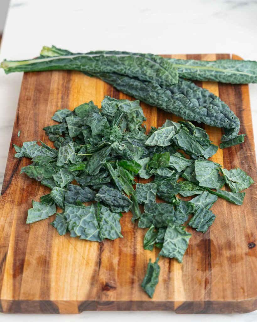 Whole and shredded lacinato kale leaves on a wooden cutting board